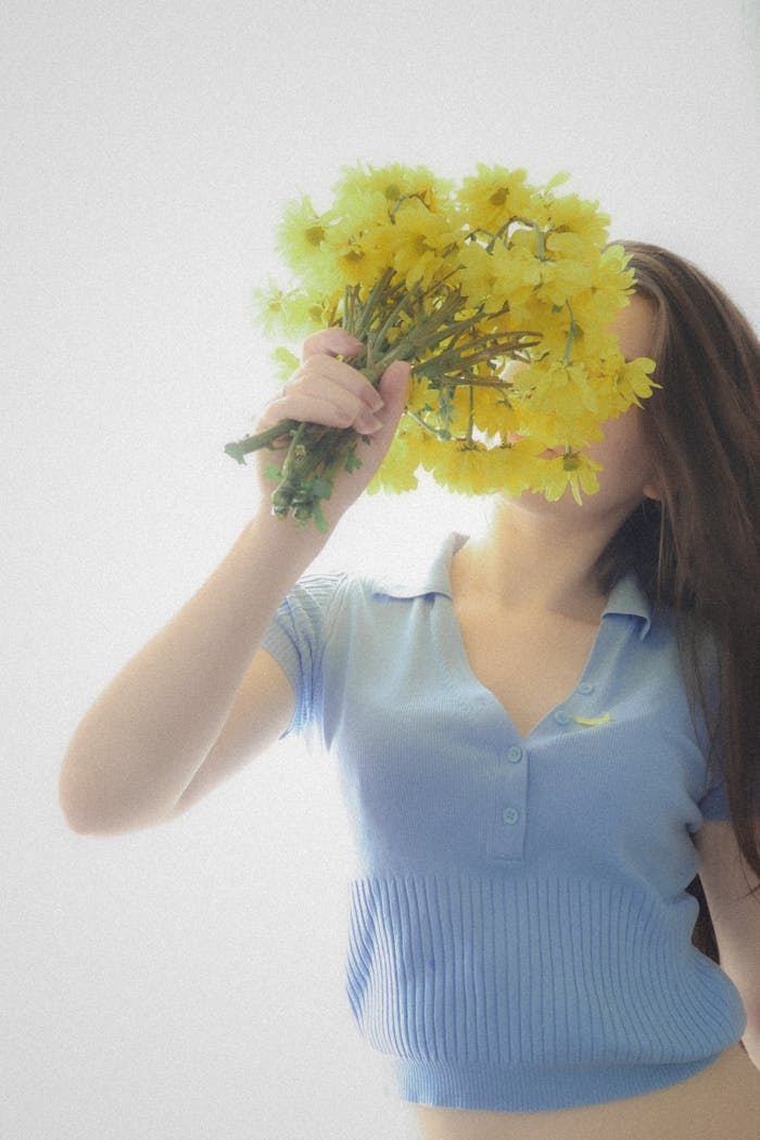 An artistic portrait of a woman holding a bouquet of yellow flowers with a soft light effect.