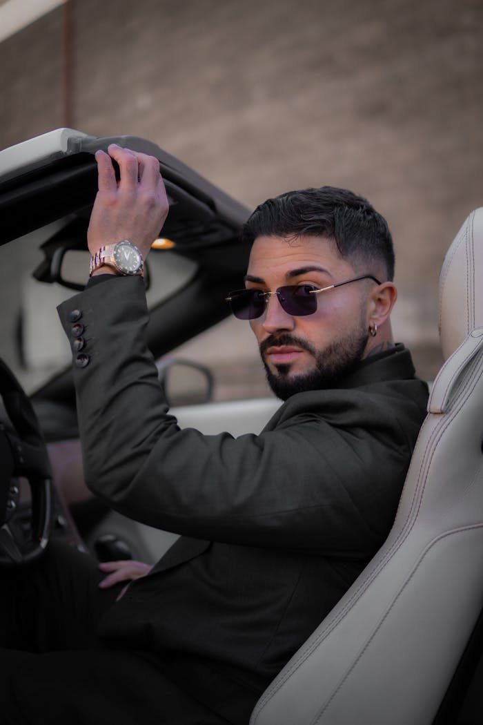 Confident man in a cabriolet wearing sunglasses and a suit, showcasing urban elegance.