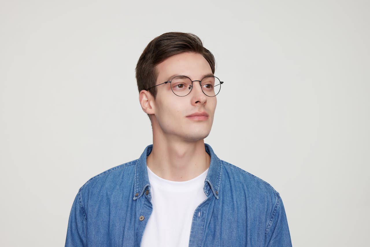 Portrait of a stylish young man in glasses wearing a denim shirt.