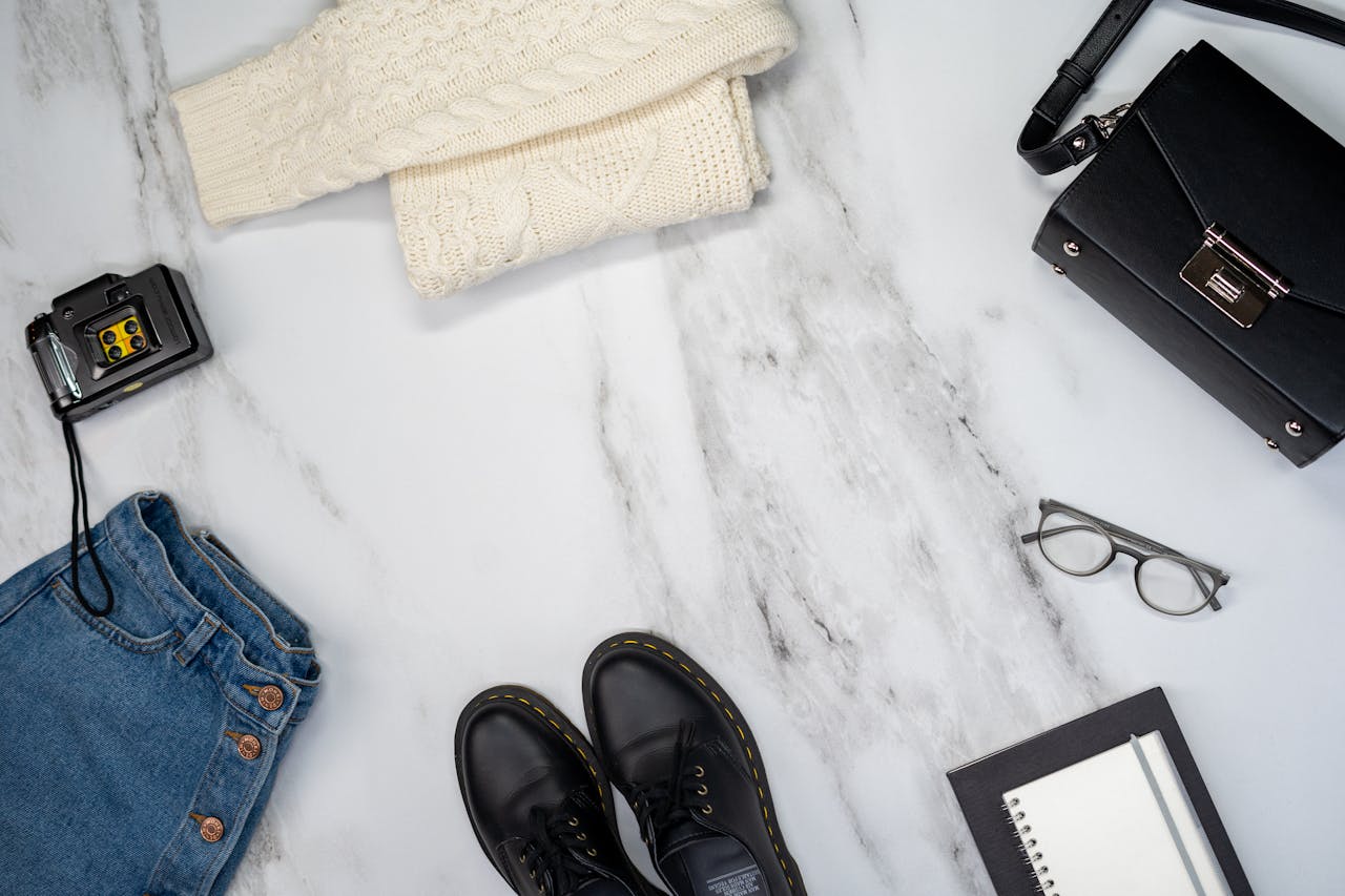 Flat lay of casual fashion items including jeans, shoes, and accessories on a marble surface.