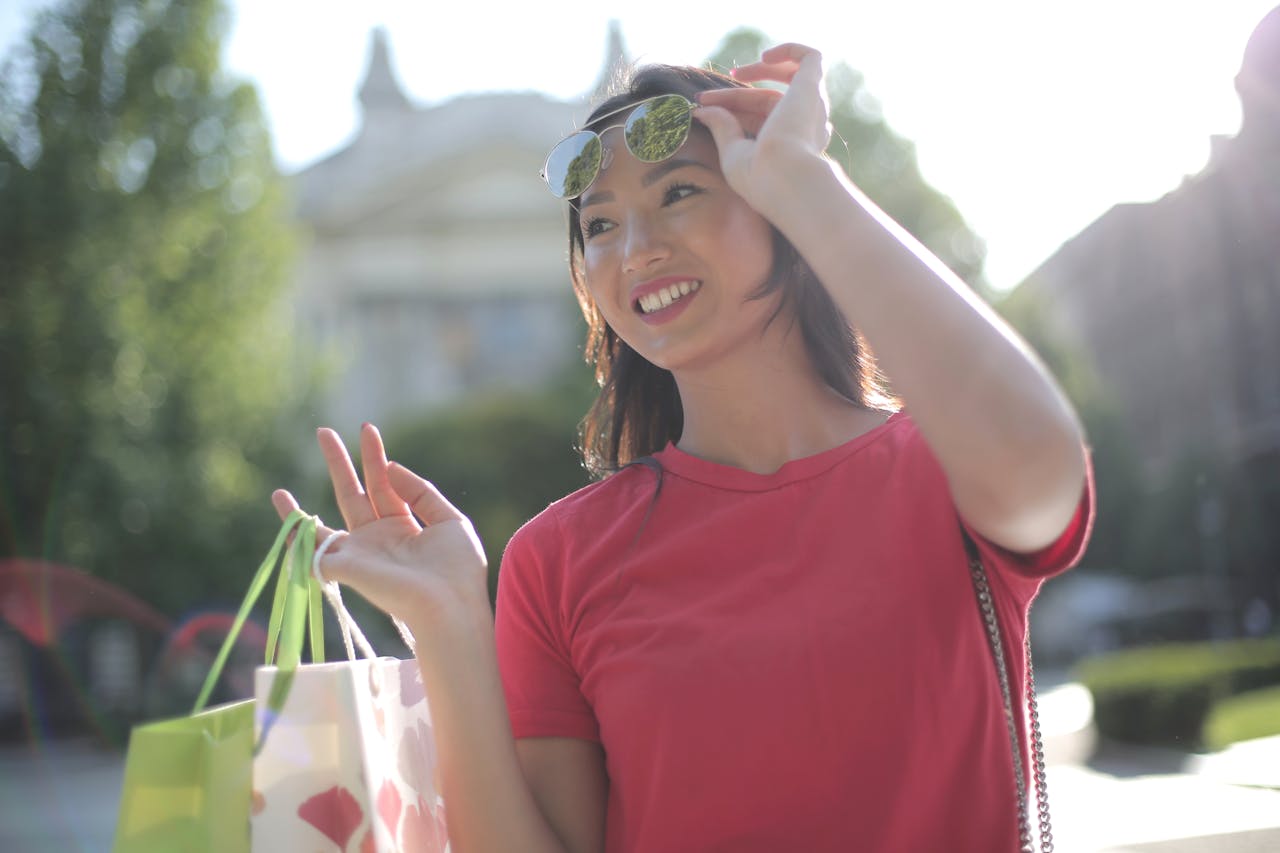 Joyful woman enjoying a shopping day in a sunny park, wearing a red t-shirt and sunglasses.
